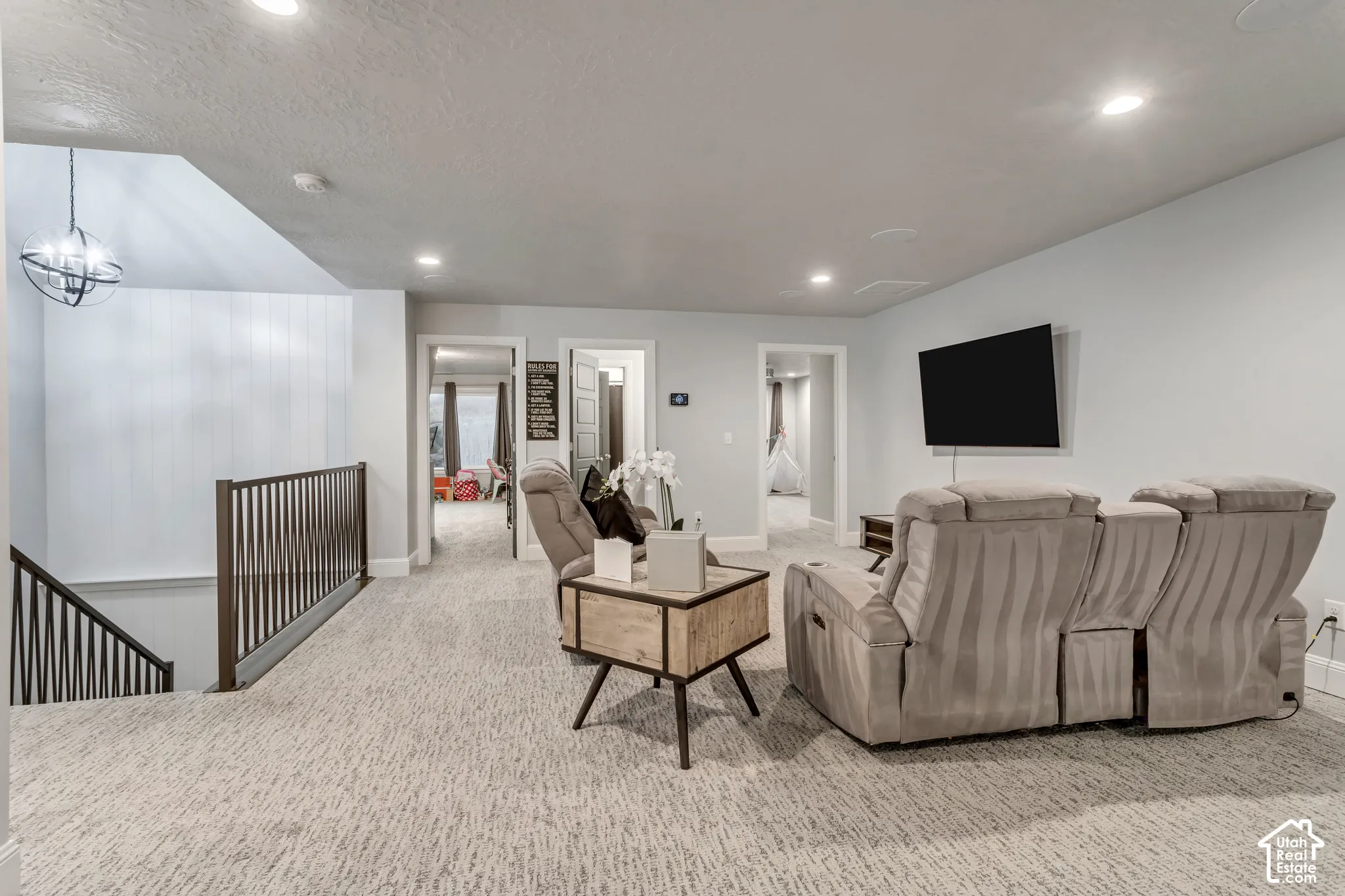 Open living space featuring recessed lighting, carpeted flooring, metal staircase railing, and a geometric pendant light fixture
