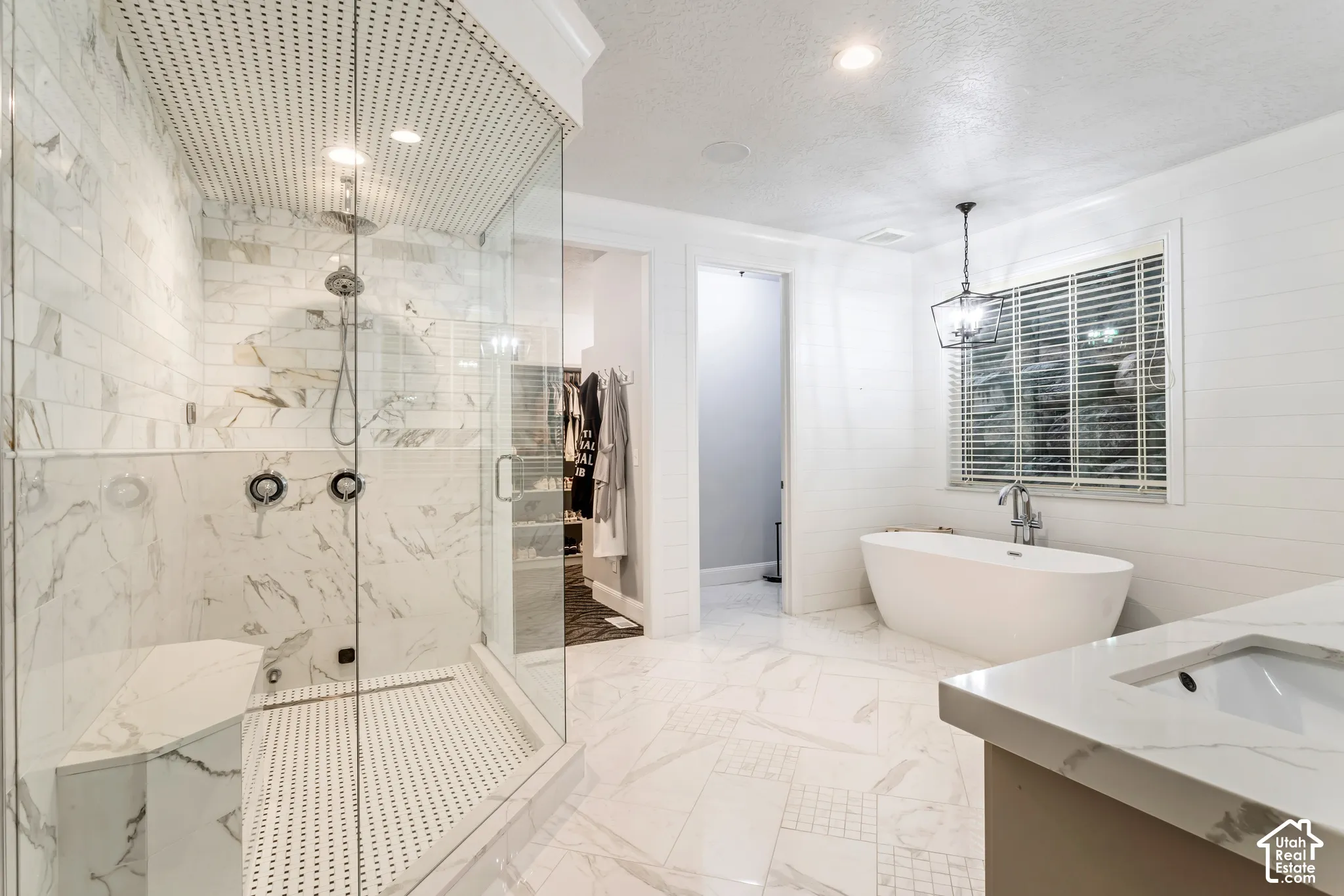 Walk-in glass shower with marble-look wall tile and integrated bench, freestanding soaking tub, dual wall-mounted shower controls, mosaic tile shower ceiling, and quartz countertop vanity