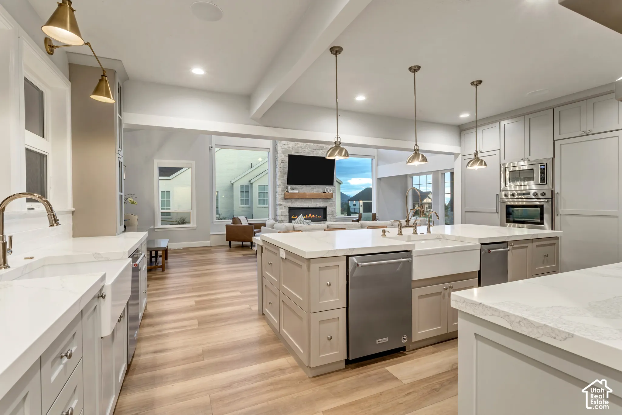 Kitchen featuring an expansive central island, farmhouse sinks, wood-finish flooring, shaker-style cabinetry, and stainless steel built-in appliances