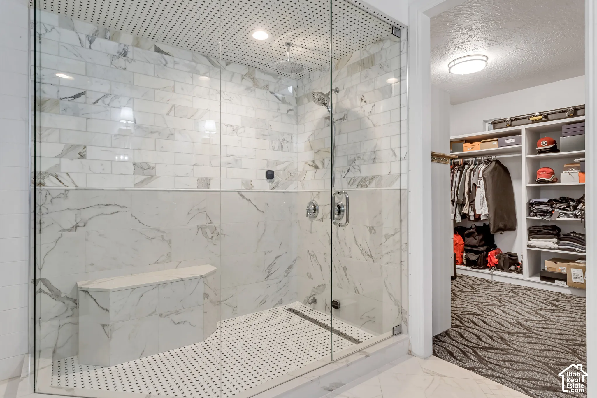 Walk-in shower featuring a glass enclosure, built-in stone-finish bench, oversized subway tile wall surround, and recessed ceiling lighting, complemented by a walk-in closet with custom built-in shelving