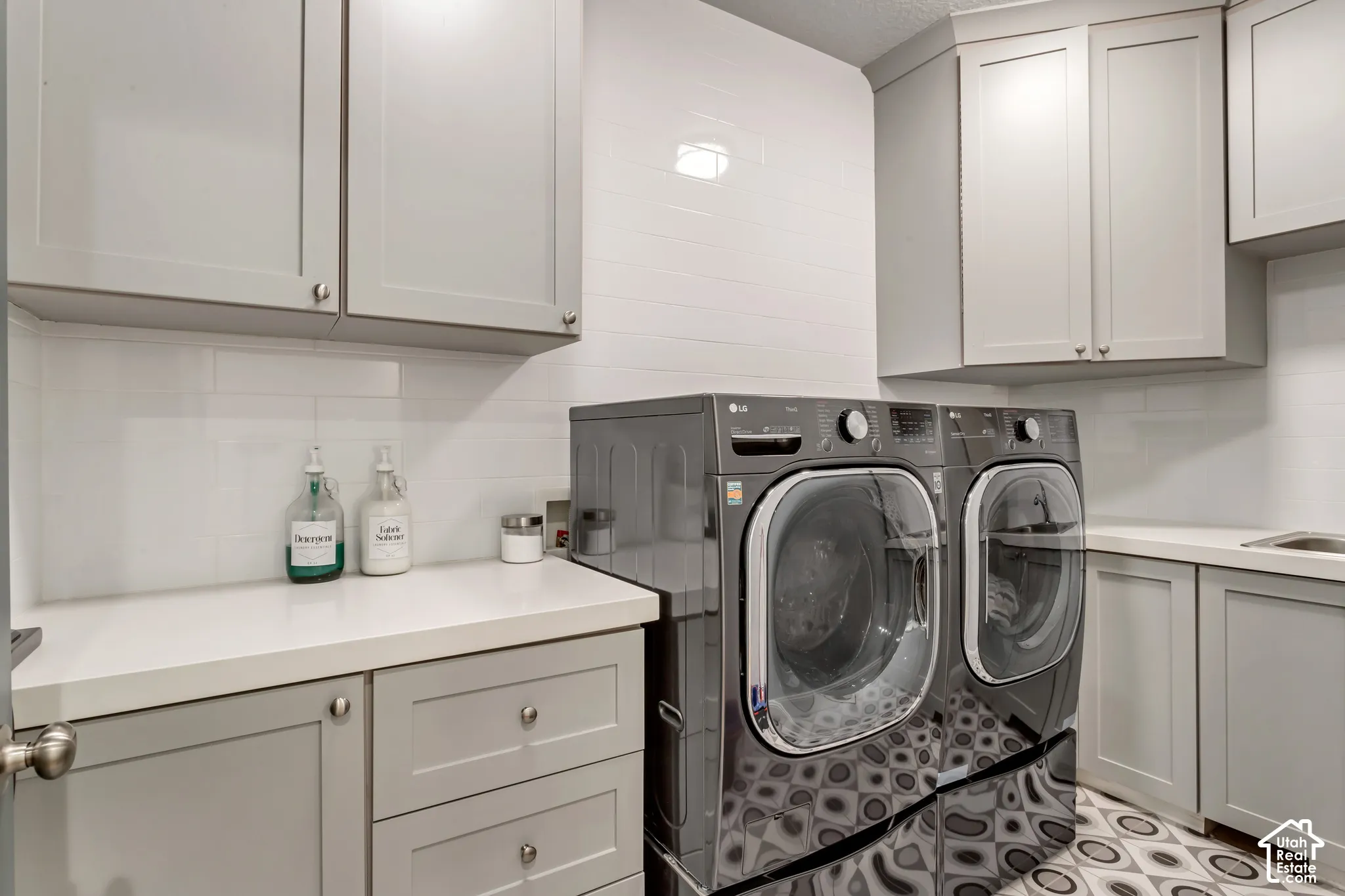 Utility room featuring grey shaker-style cabinetry, white solid-surface countertops, white subway tile backsplash, and patterned tile flooring