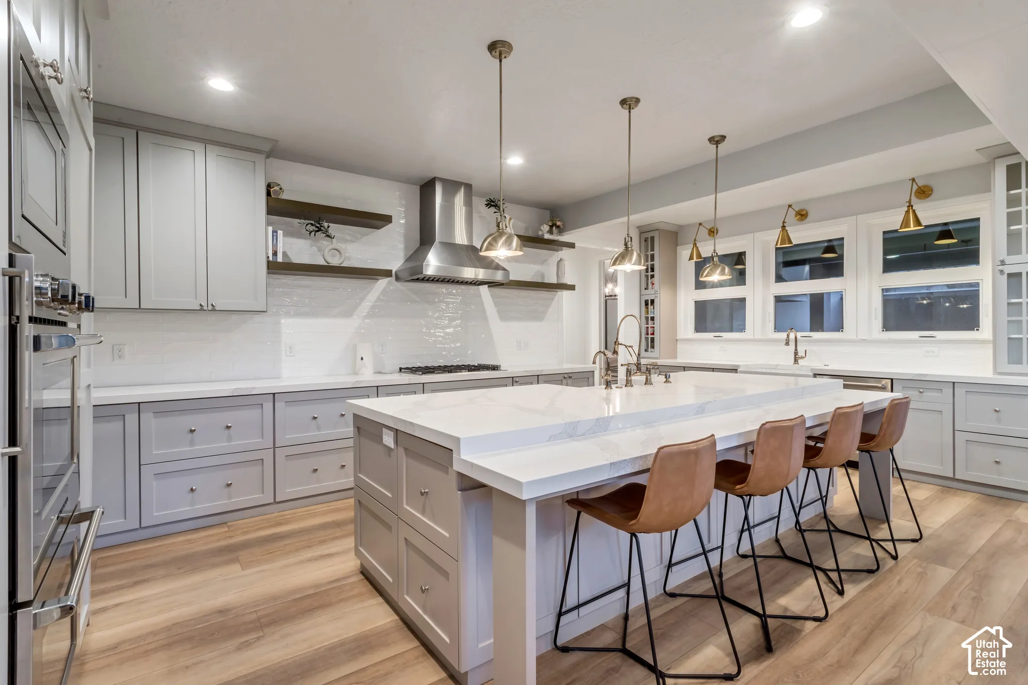 Kitchen featuring custom cabinetry, waterfall-edge stone island, stainless steel range hood, built-in dual oven, and wood-finish flooring