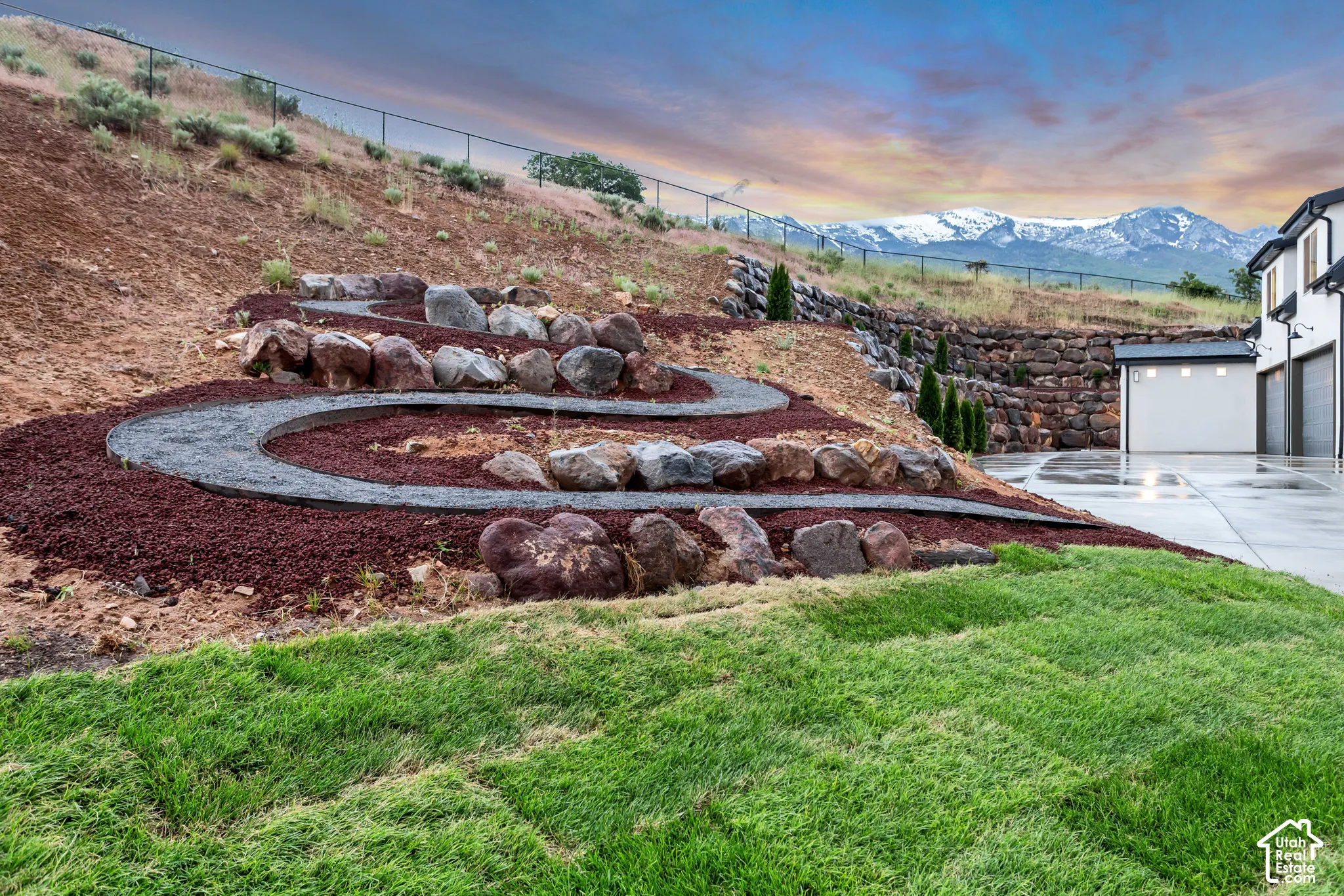Terraced hillside landscaping featuring natural stone retaining walls, gravel pathways, mulch ground cover, and a mountainous backdrop