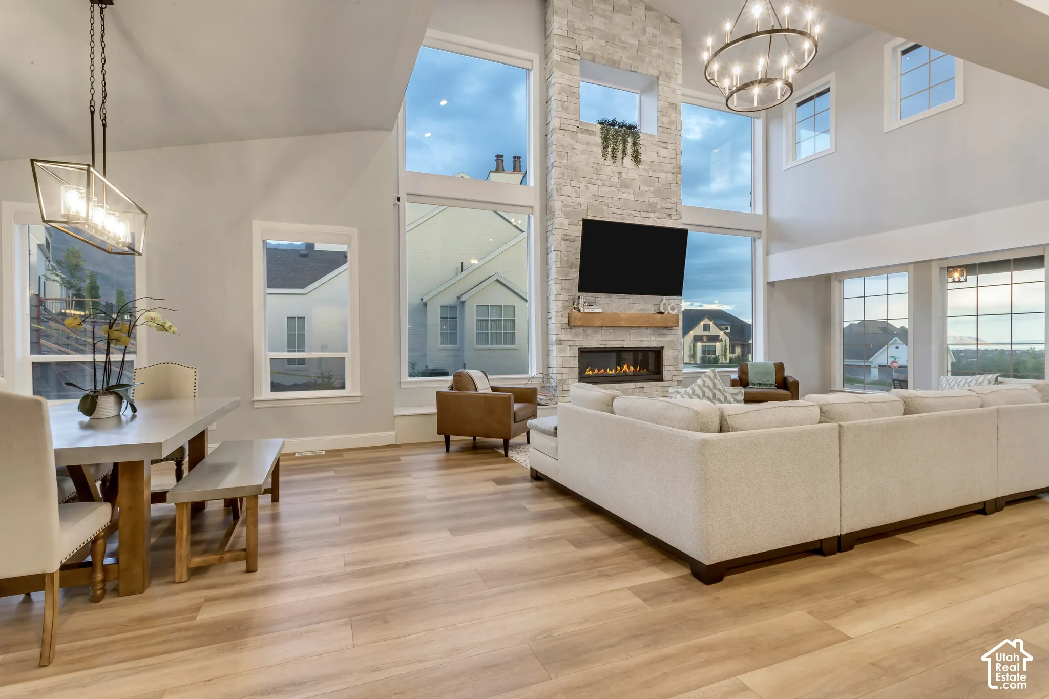Vaulted ceilings featuring expansive multi-story windows, full-height stacked-stone fireplace, linear built-in gas firebox, timber mantel, and wood-finish flooring