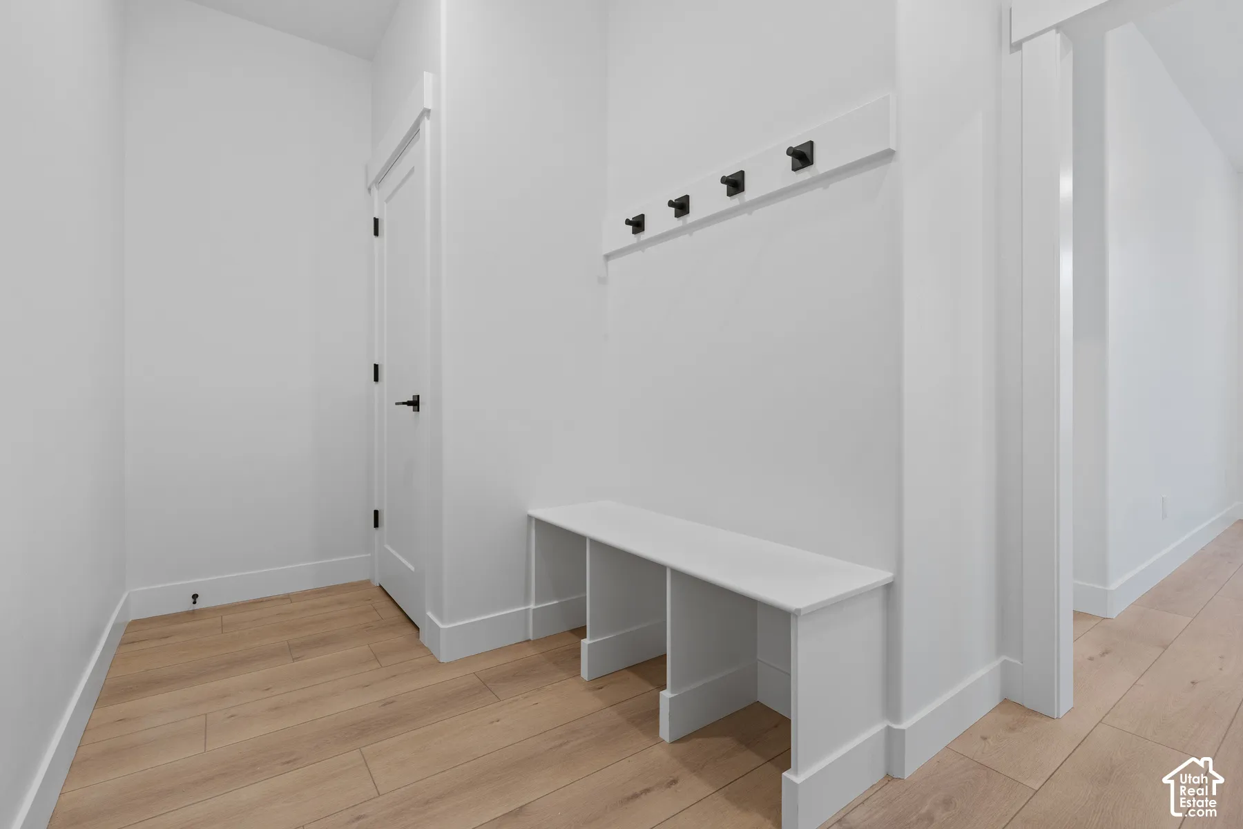 Built-in white storage bench with integrated shelving and wall-mounted matte black coat hooks over wood-finish flooring