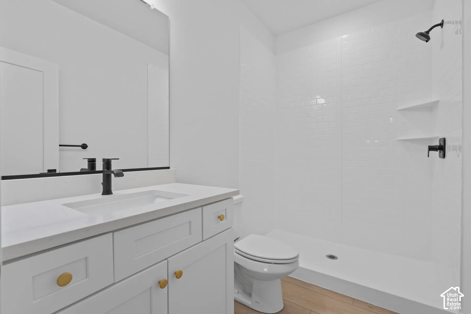 White vanity featuring a quartz countertop, rectangular under-mount sink, and matte black faucet, paired with a shower stall featuring white subway tile walls, built-in shelving, and a matte black shower head