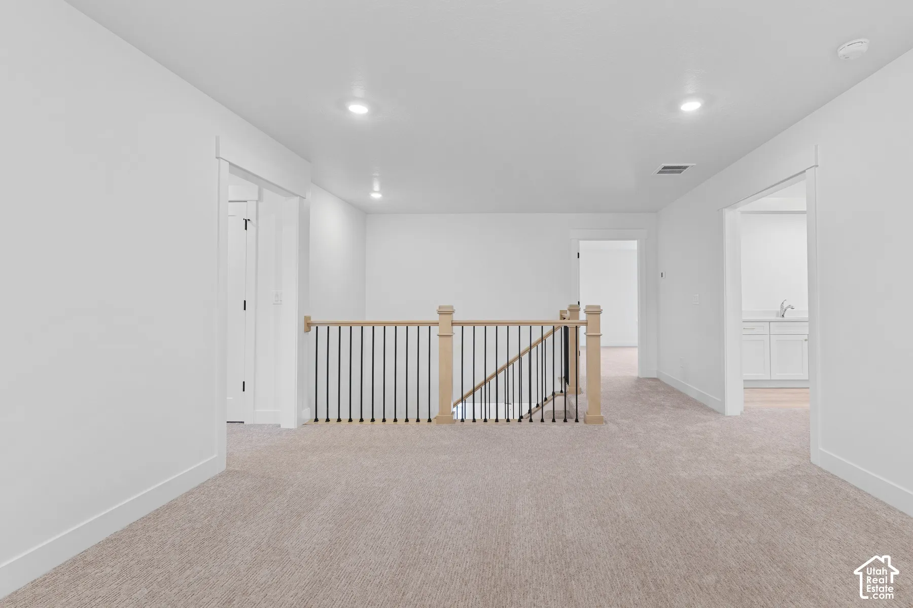 Open landing area featuring neutral carpeting, recessed ceiling lighting, and a staircase railing with wood posts and metal balusters