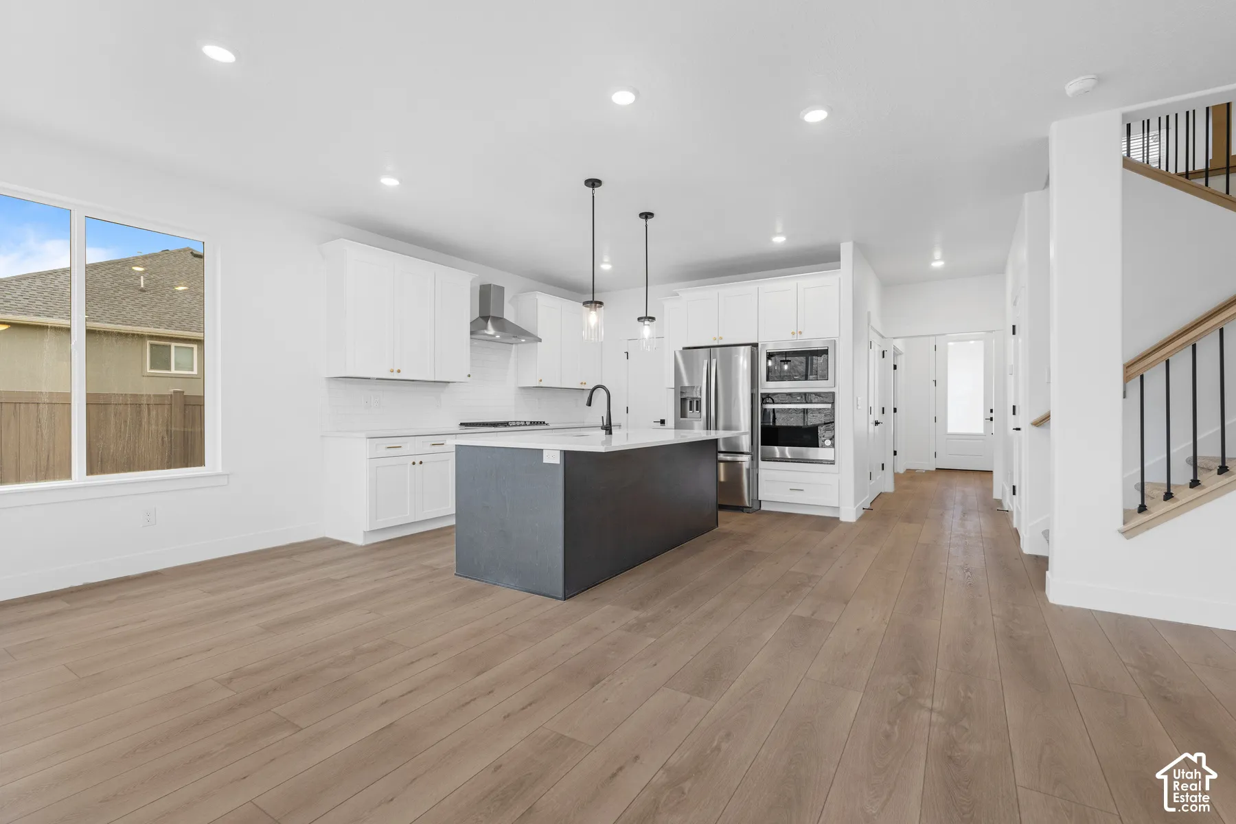 Kitchen featuring white shaker-style cabinetry, a contrasting dark-toned kitchen island with a white countertop, stainless steel built-in appliances, recessed lighting, and wood-finish flooring