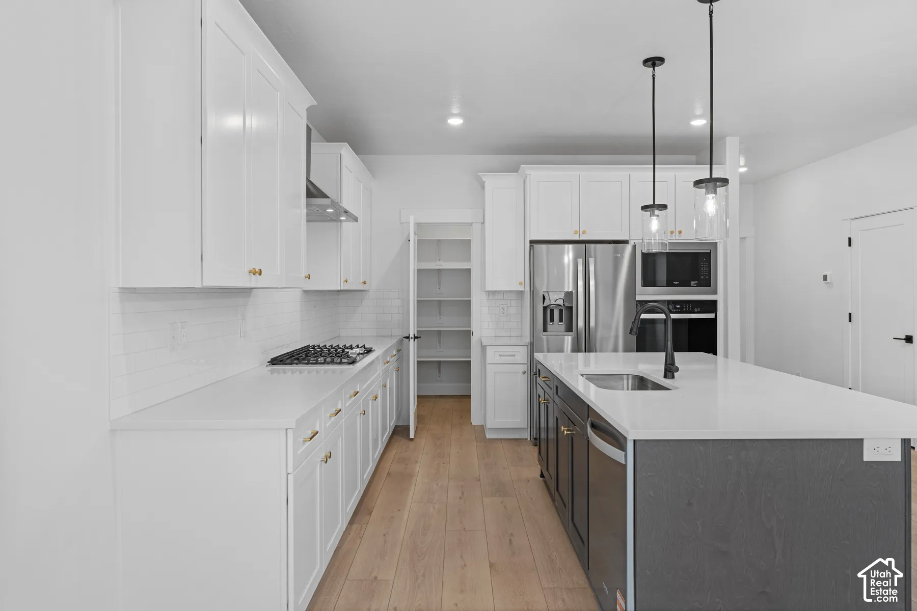 Kitchen featuring white cabinetry, quartz countertops, a central island with a contrasting dark finish, wood-finish flooring, and a walk-in pantry