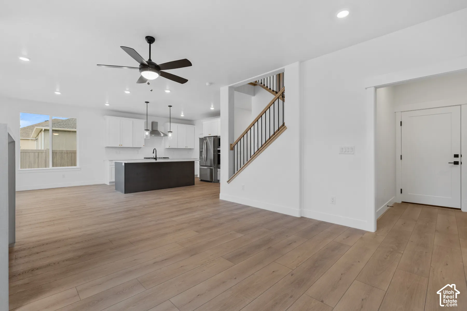 Open floor plan featuring wood-finish flooring, a kitchen island with stone-finish countertops, recessed lighting, and a staircase with metal balusters