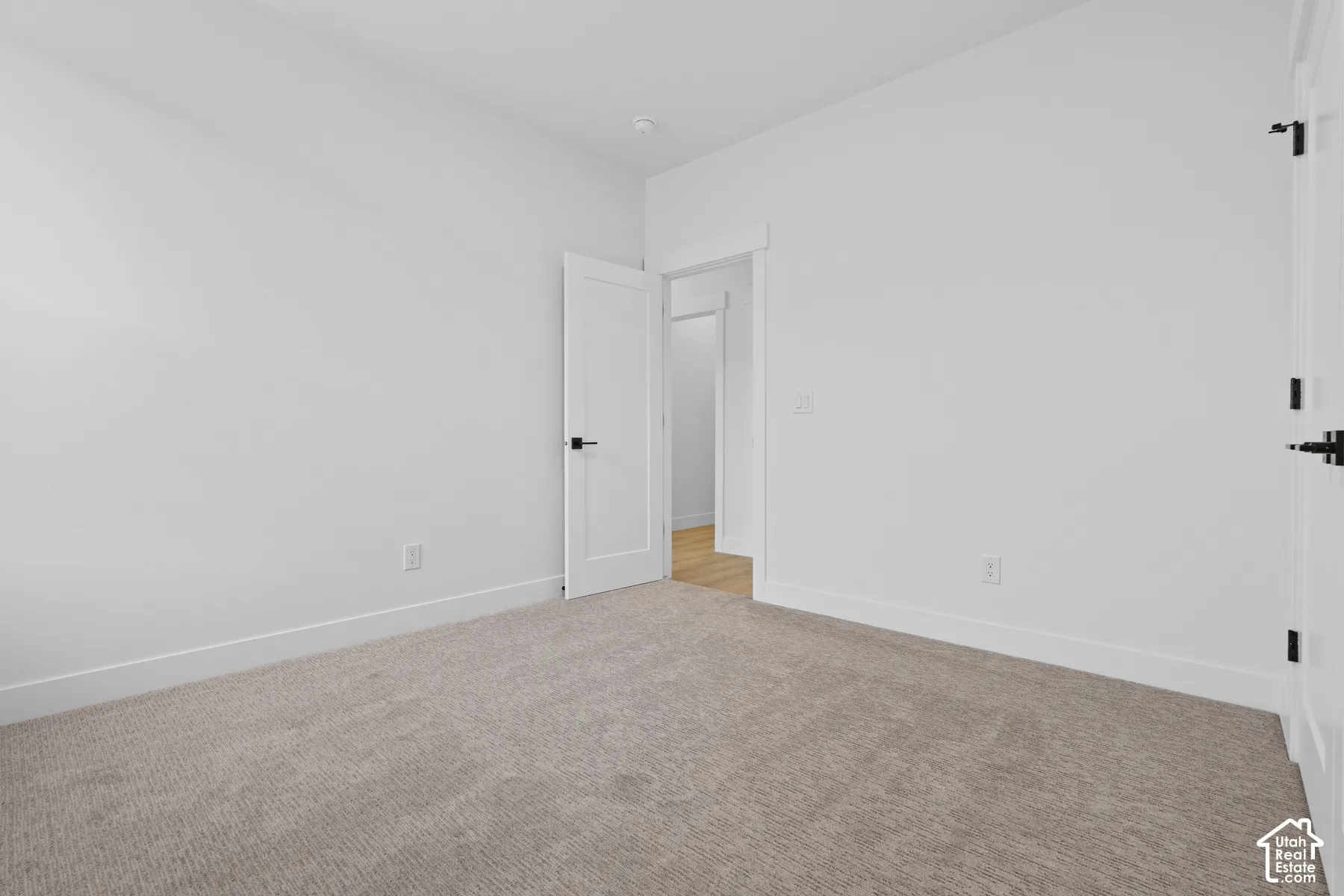 Neutral wall color, plush wall-to-wall carpeting, white shaker-style interior doors, and matte black lever hardware