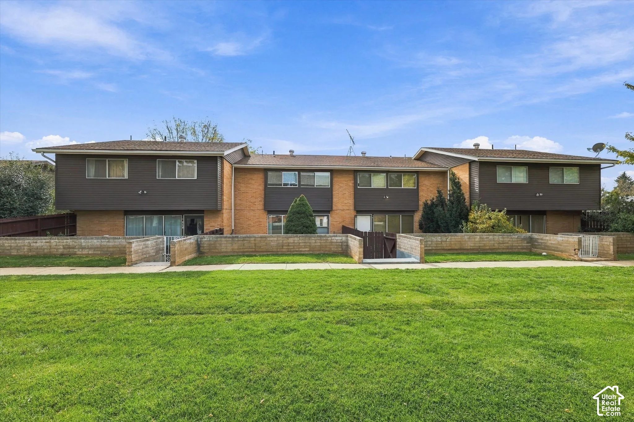 Multi-unit structure featuring brick and horizontal siding exterior, low-slope rooflines, and private masonry-walled patio enclosures