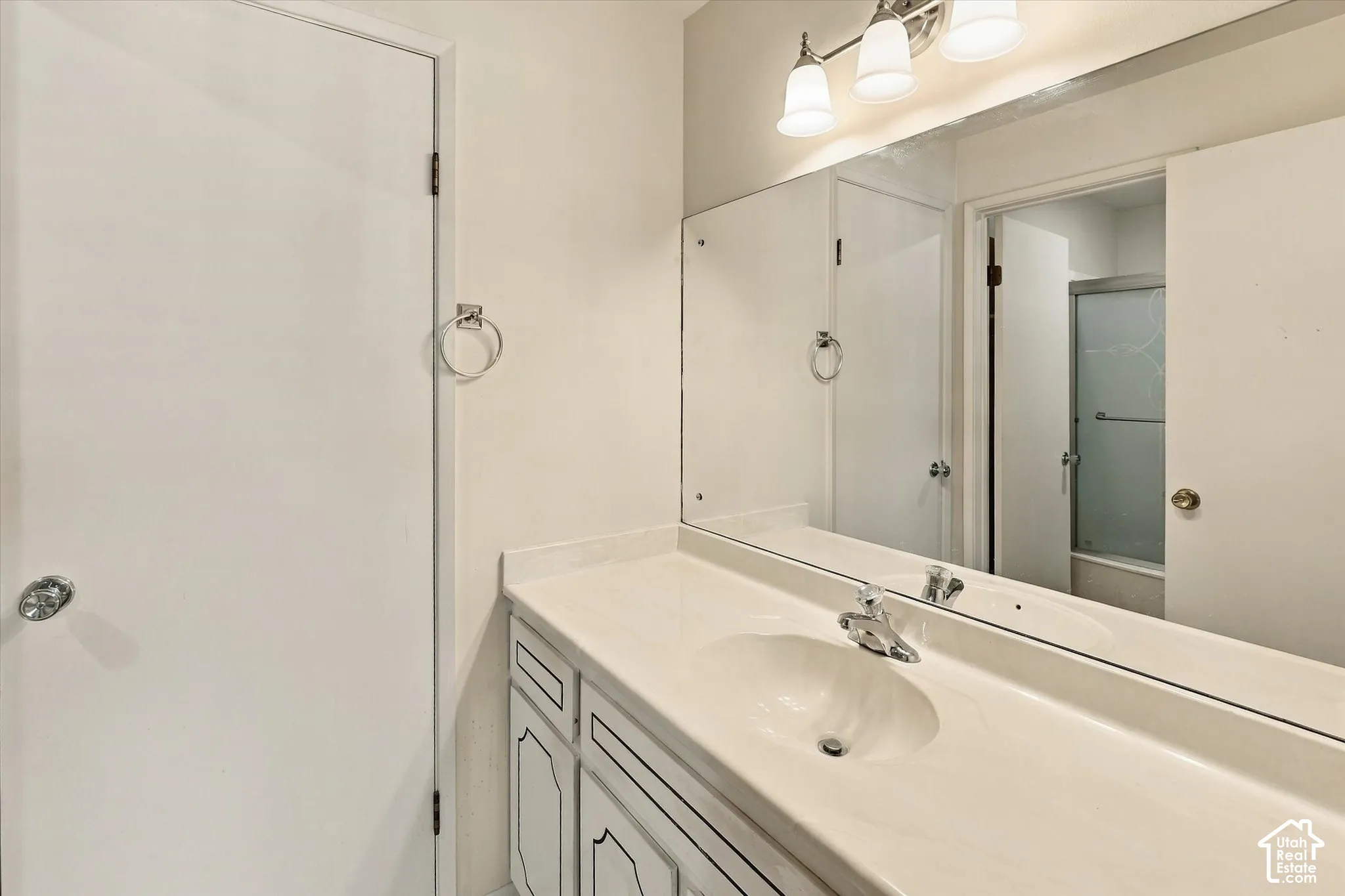 Vanity featuring an integrated sink, solid-surface countertop, white cabinetry with decorative trim, a full-width mirror, and a three-light fixture
