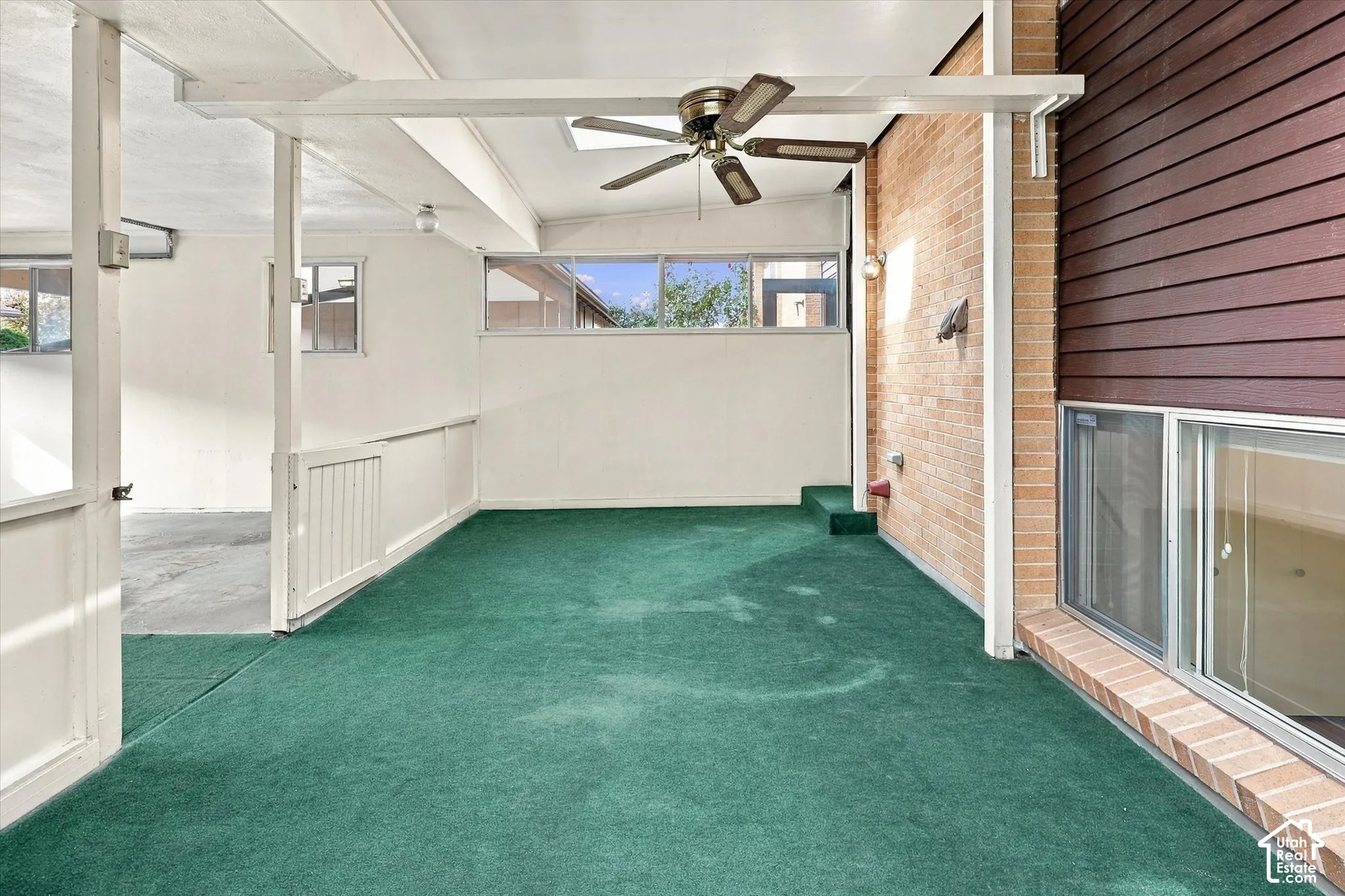 Covered patio featuring an exposed brick wall, horizontal wood-finish siding, a ceiling fan, and horizontal clerestory windows