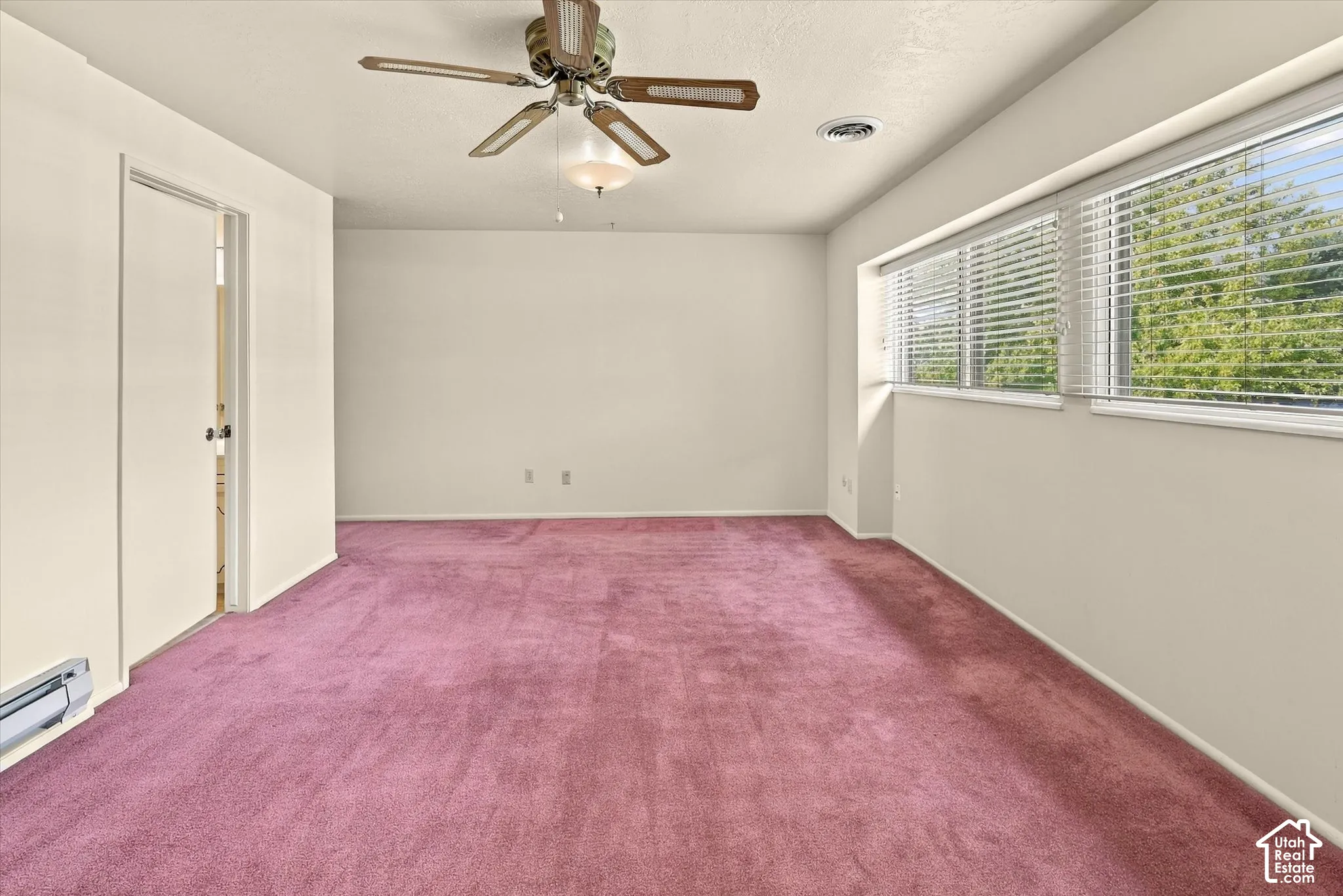 Room featuring wall-to-wall carpeting, wide horizontal windows with integrated blinds, and a ceiling fan with integrated lighting