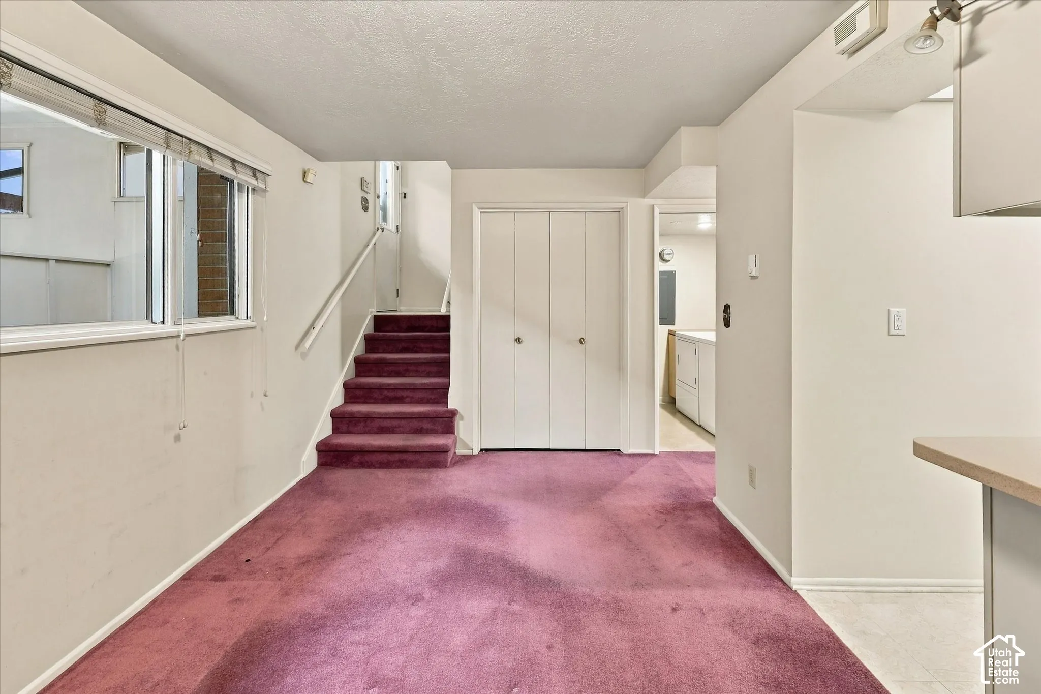 Carpeted interior featuring bi-fold closet doors, a staircase with a handrail, and a window with a horizontal blind