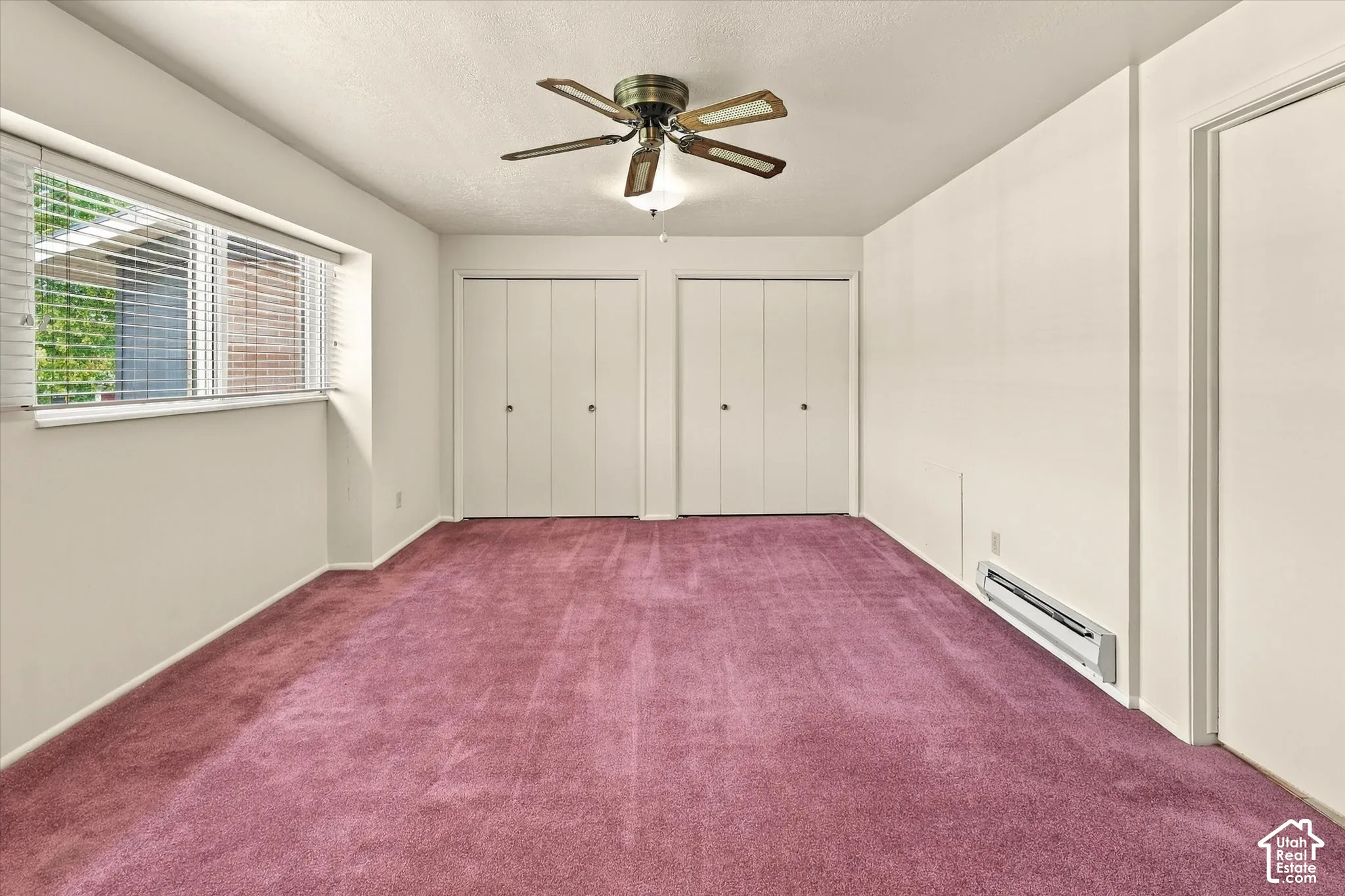 Interior space featuring wall-to-wall carpeting, dual closets with bifolder doors, a ceiling fan with integrated lighting, and a window with horizontal blinds
