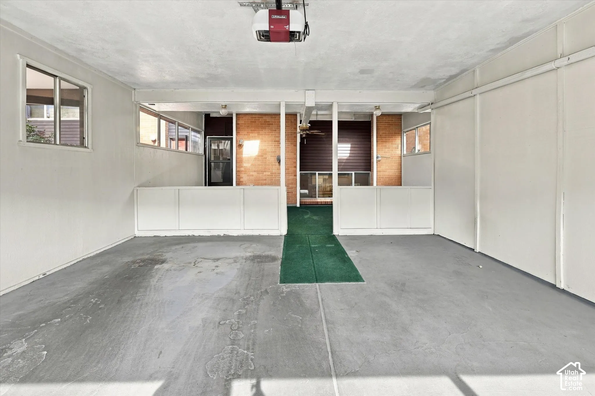 Enclosed garage featuring exposed brick wall accents, multiple windows, built-in lower-wall storage cabinetry, and a ceiling-mounted automatic door opener