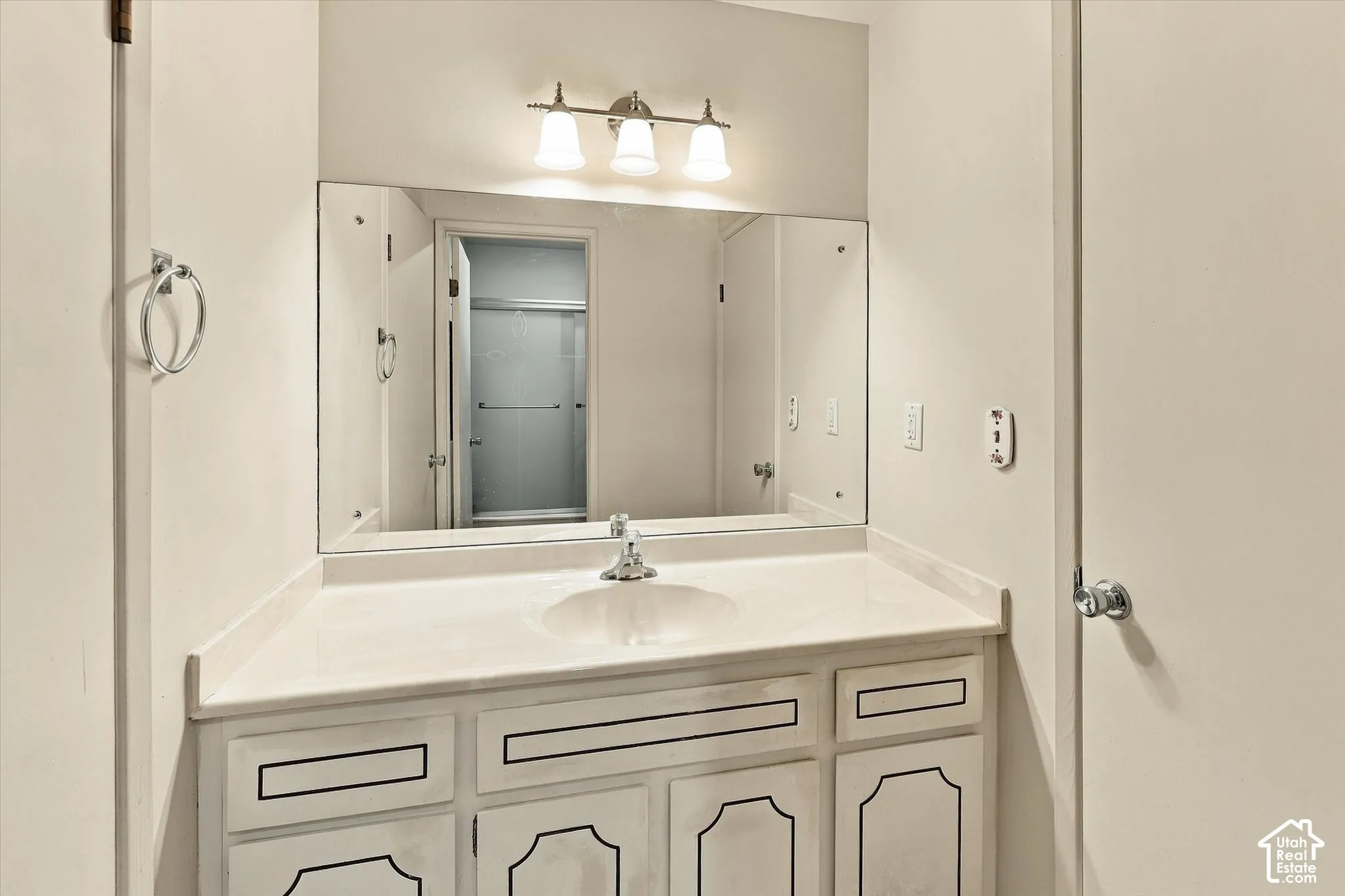 Bathroom vanity featuring a solid-surface countertop with an integrated basin, white cabinetry with decorative trim, a full-width wall mirror, and a three-light vanity fixture