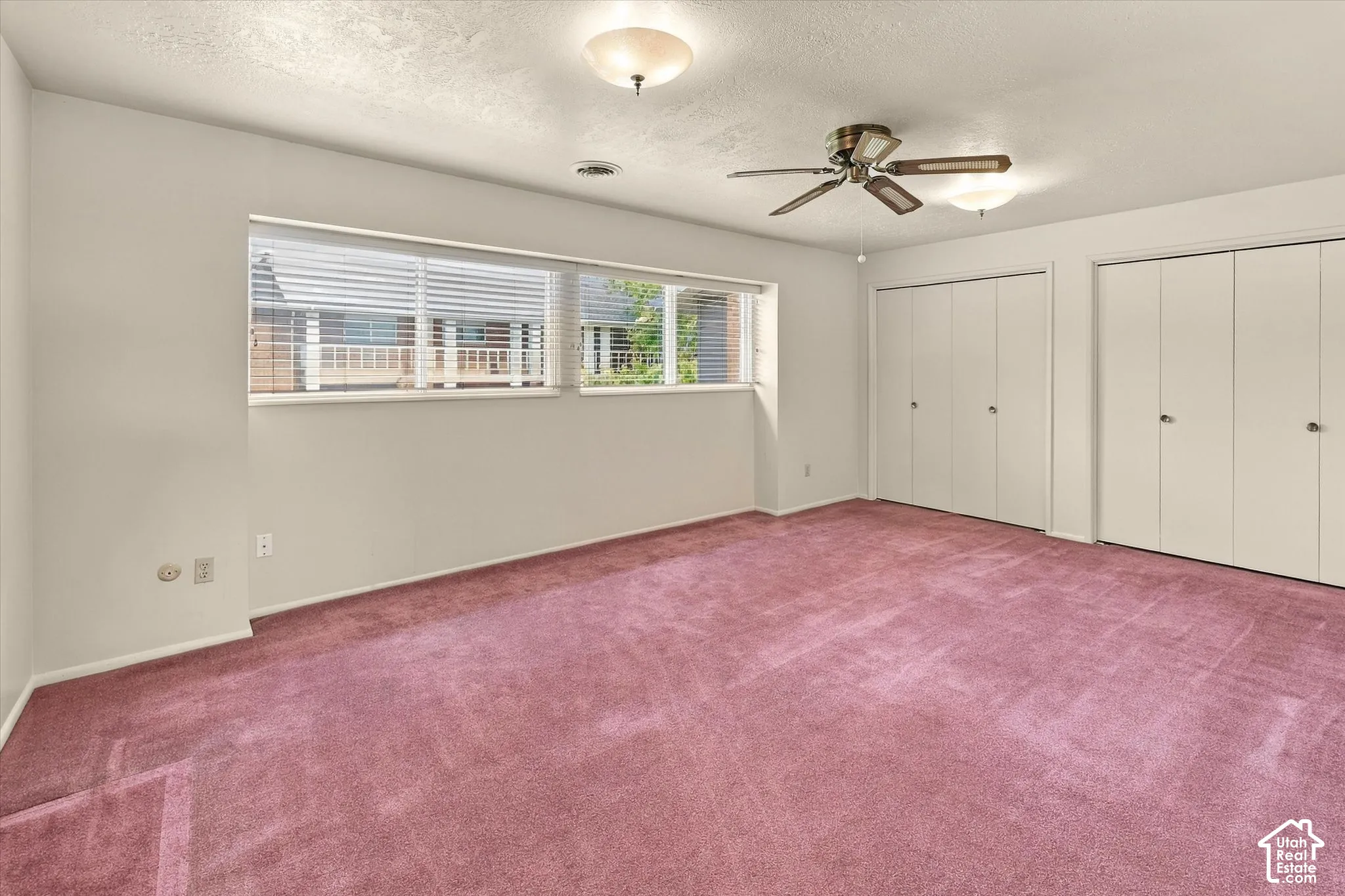 Carpeted flooring, dual floor-to-ceiling closets with paneled doors, ceiling fan with integrated lighting, and expansive horizontal windows