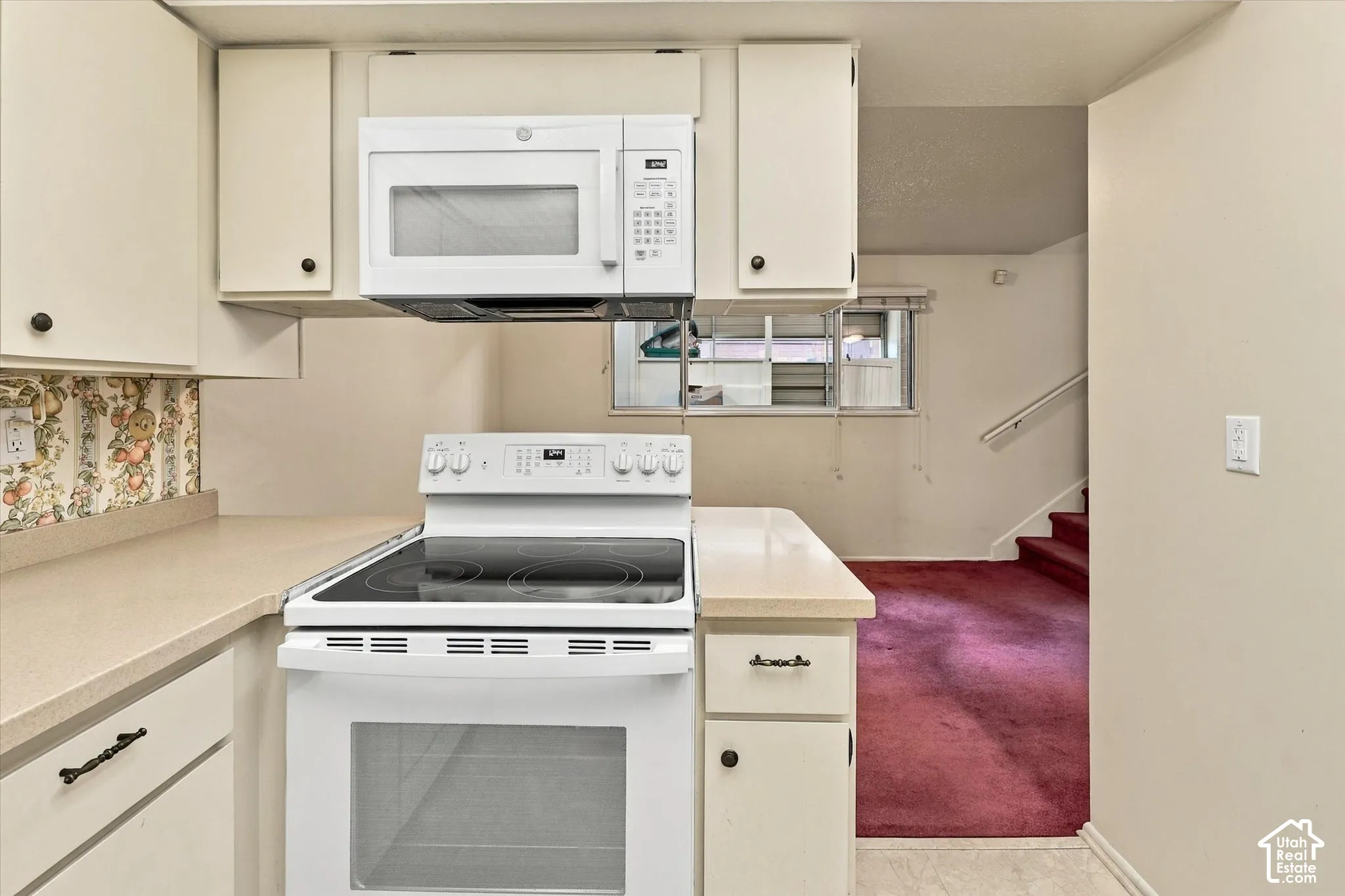 Kitchen featuring white cabinetry, neutral countertops, a built-in over-the-range microwave, and an electric range