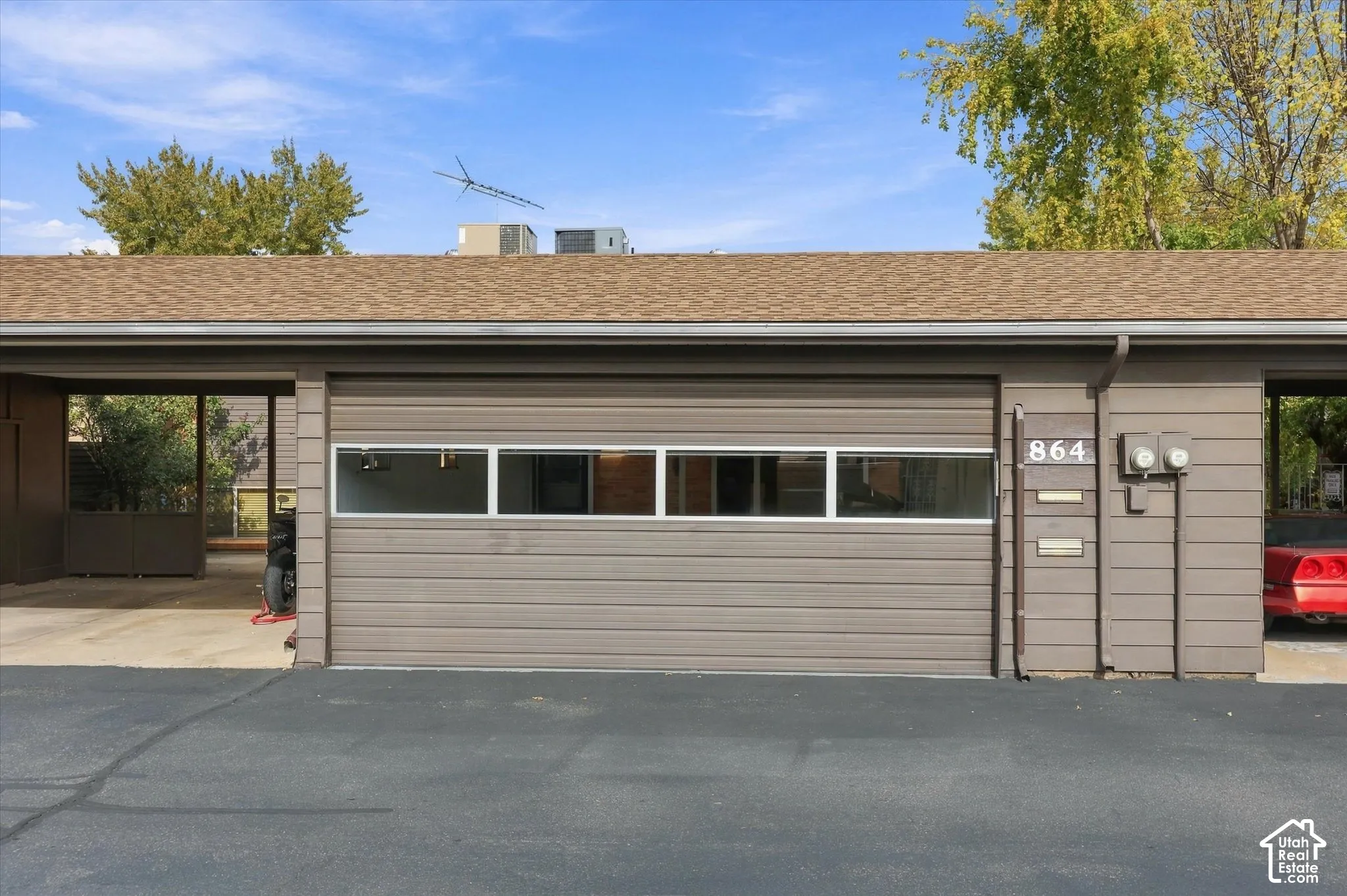Exterior featuring a single-car garage with a horizontal-panel door and a horizontal clerestory window row, wood-siding facade, asphalt shingle roofing, and an integrated carport area