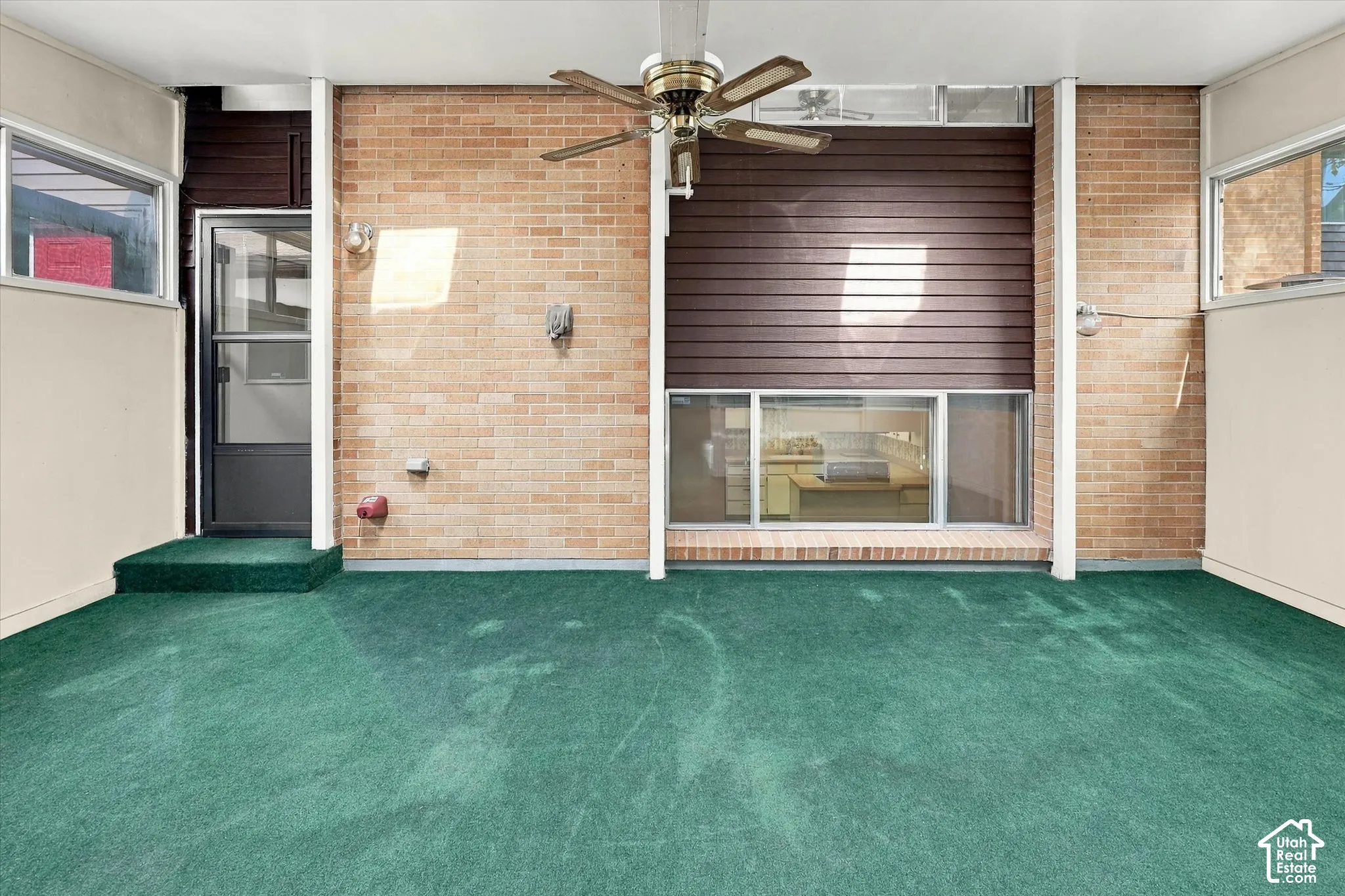 Covered patio featuring brick masonry walls, horizontal wood-panel siding, large windows, and a ceiling-mounted fan