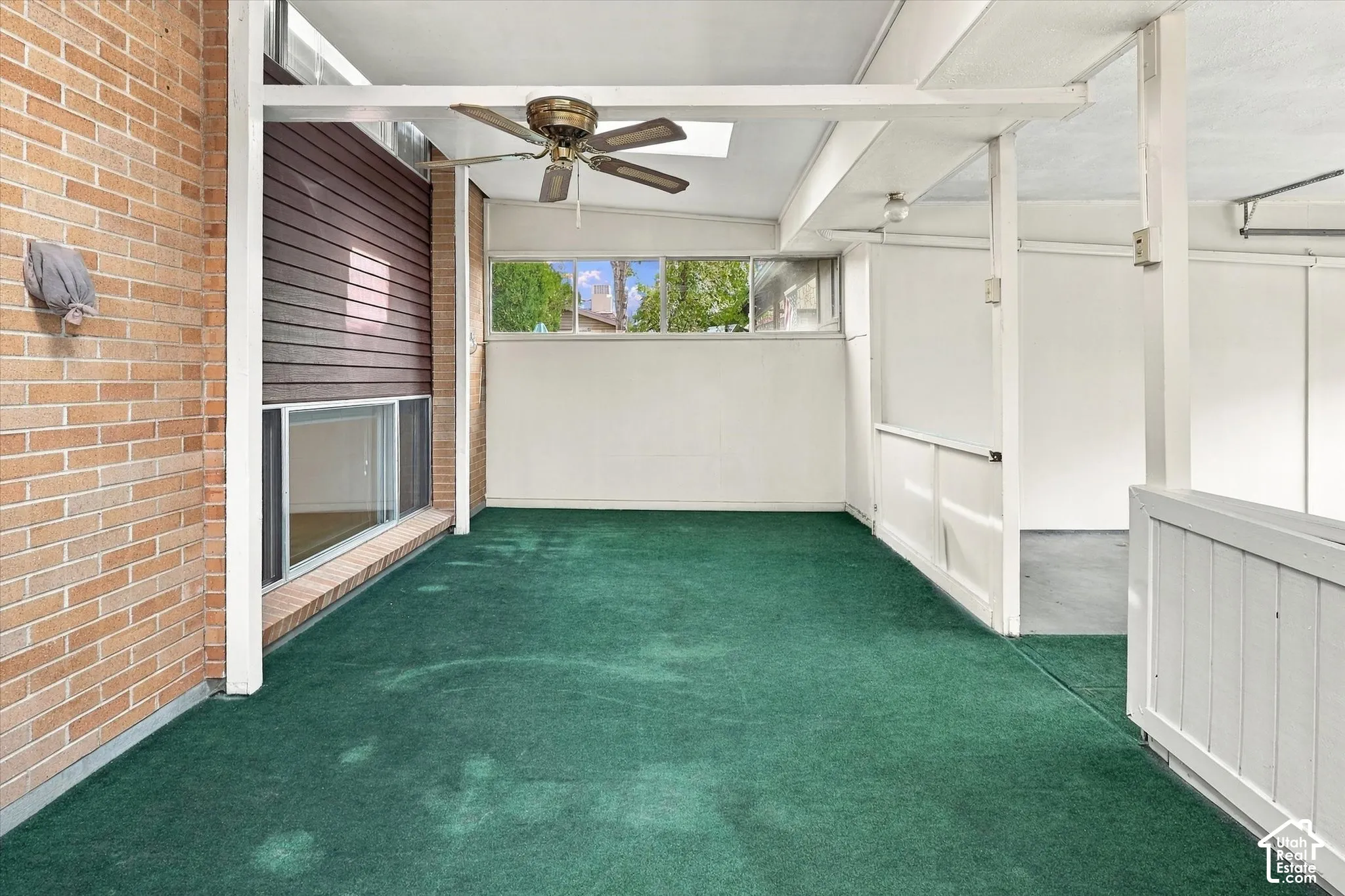 Covered patio featuring an exposed brick wall, horizontal wood-panel siding, large multi-pane windows, and a ceiling fan