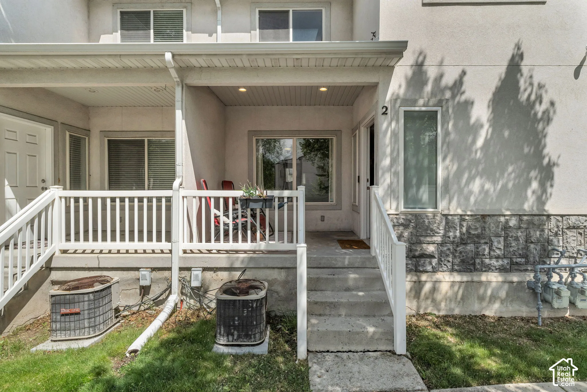 Stucco and stone veneer exterior featuring a covered front porch, white railing, and recessed ceiling lighting