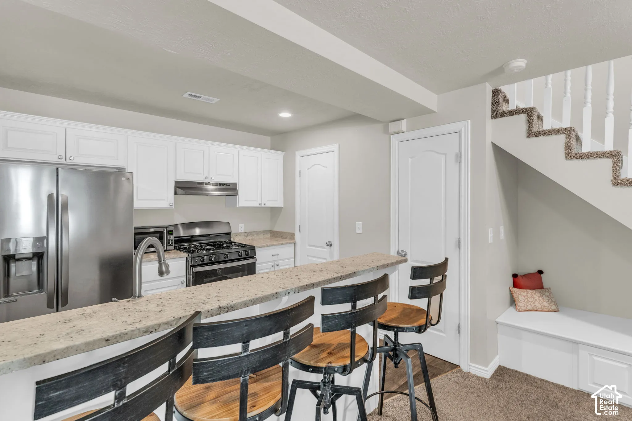 Kitchen featuring white cabinetry, stone-finish countertops, stainless steel appliance suite, and built-in under-stair bench seating