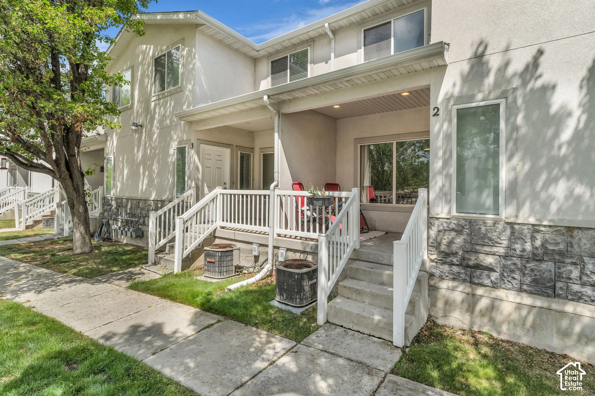 Stucco and stone veneer exterior featuring a covered porch with white railing, concrete steps, and recessed lighting