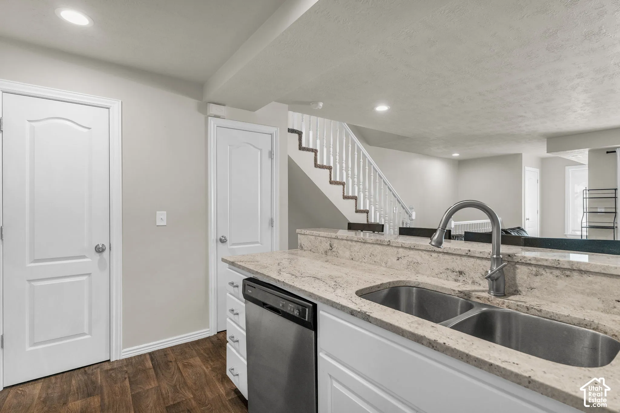 Kitchen featuring stone-finish countertops, stainless steel dual-basin sink with a pull-down faucet, white cabinetry, integrated dishwasher, and wood-finish flooring