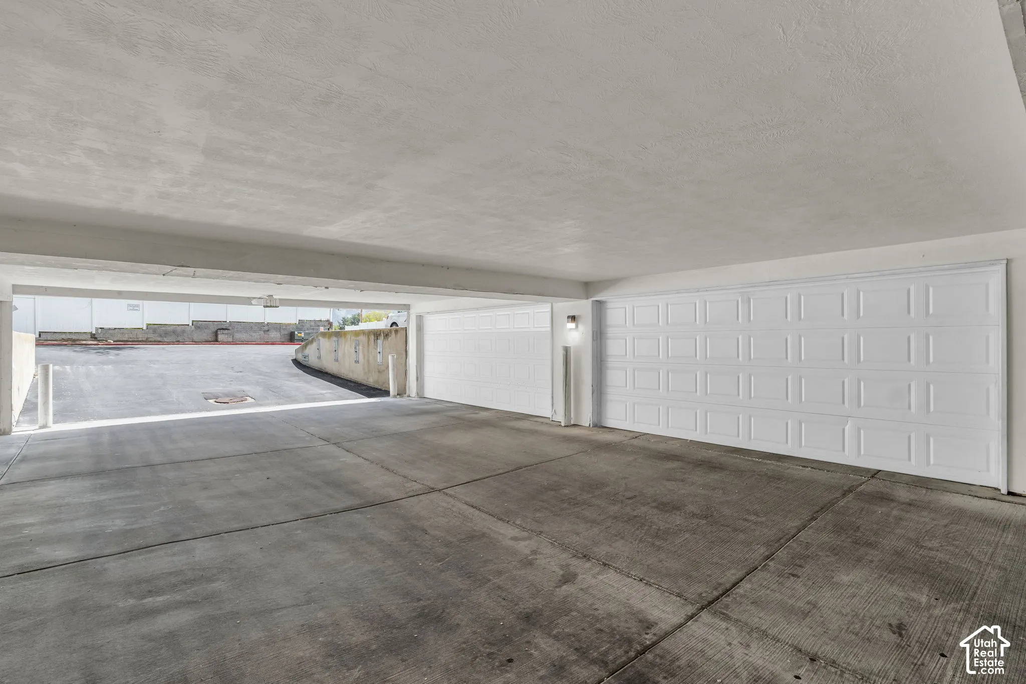 Covered multi-car garage featuring a concrete floor, white paneled sectional doors, and a reinforced concrete ceiling