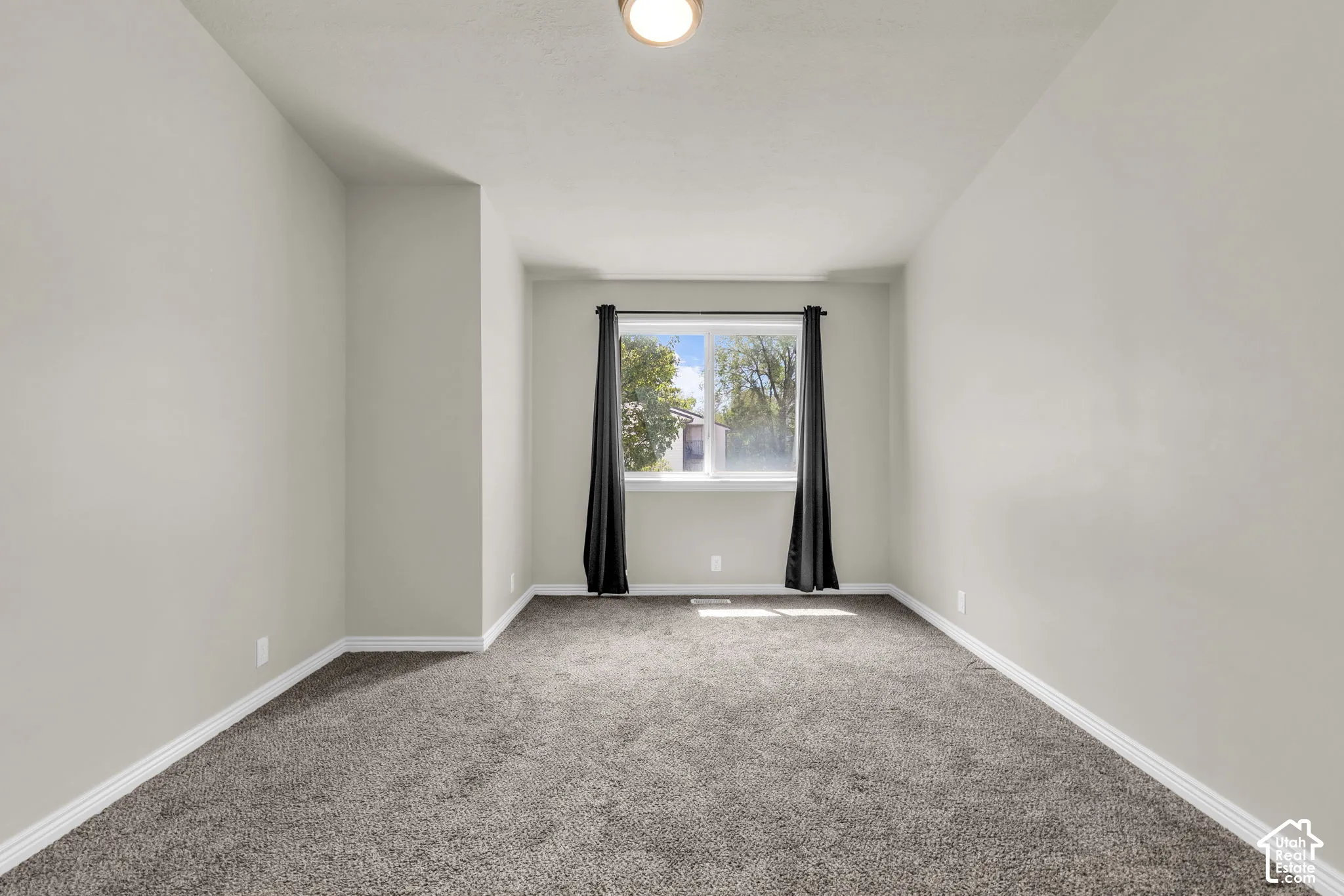 Neutral-toned interior space featuring plush carpeting, soft gray wall paint, and a large central window