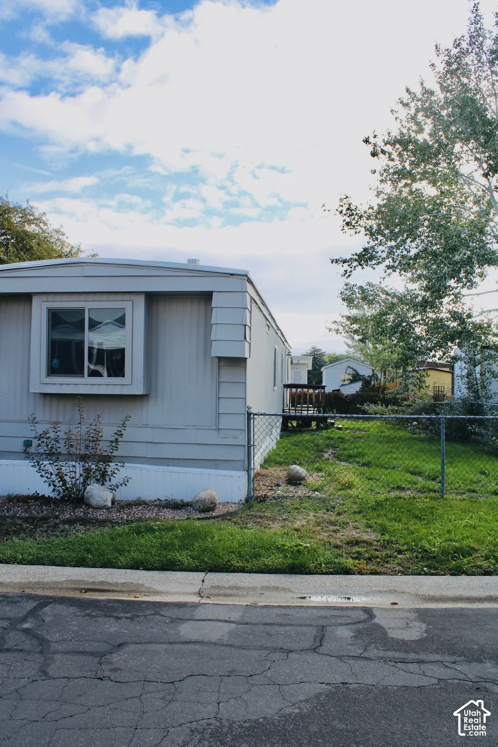Exterior featuring light-toned horizontal siding, a bay window, a wooden deck, and chain-link perimeter fencing