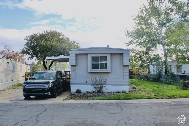 Single-level exterior featuring light-toned vertical siding, a covered carport, and a chain-link fenced perimeter