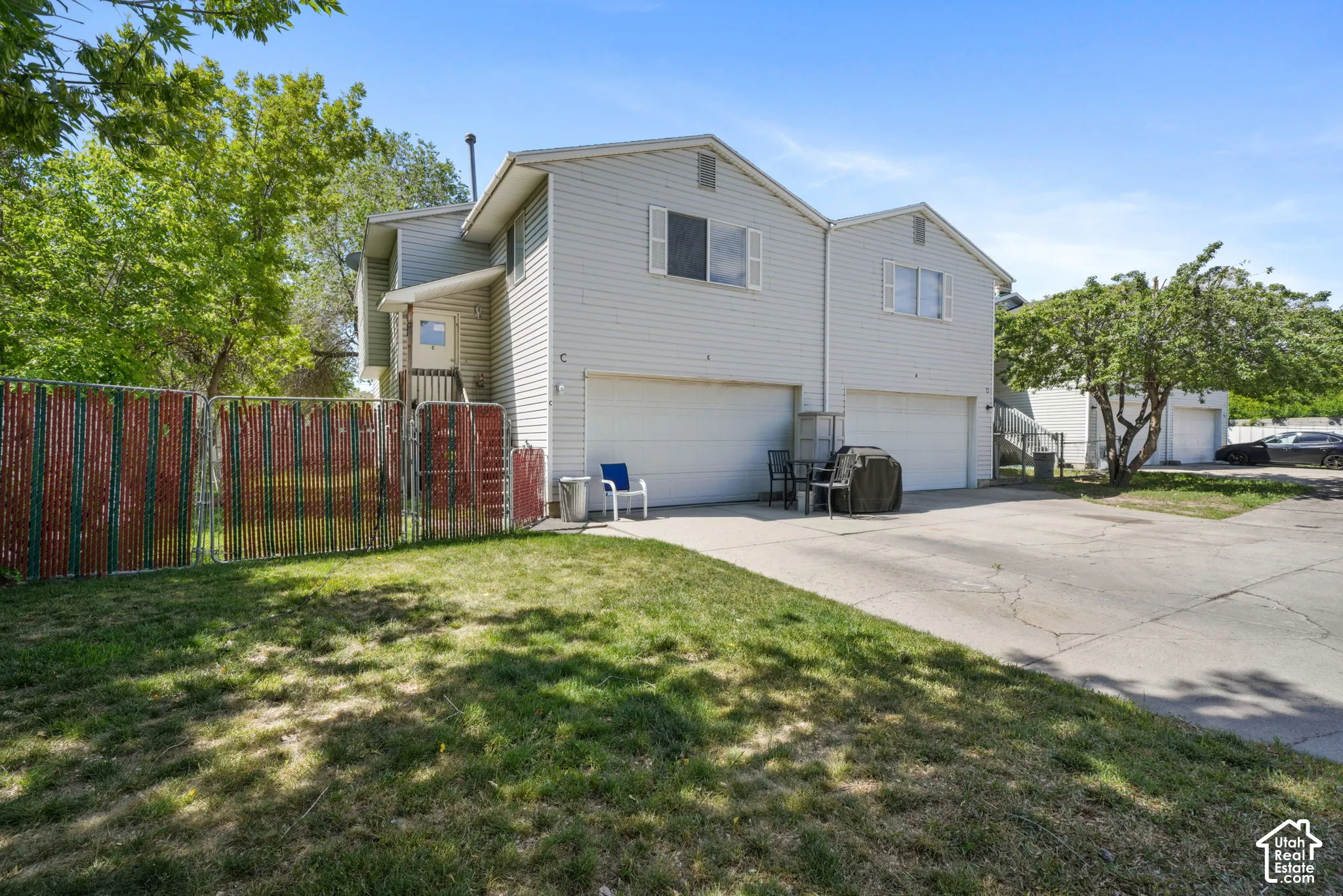 Two-story residential structure featuring light-colored horizontal siding, dual attached garages, a concrete driveway, and a chain-link fenced yard