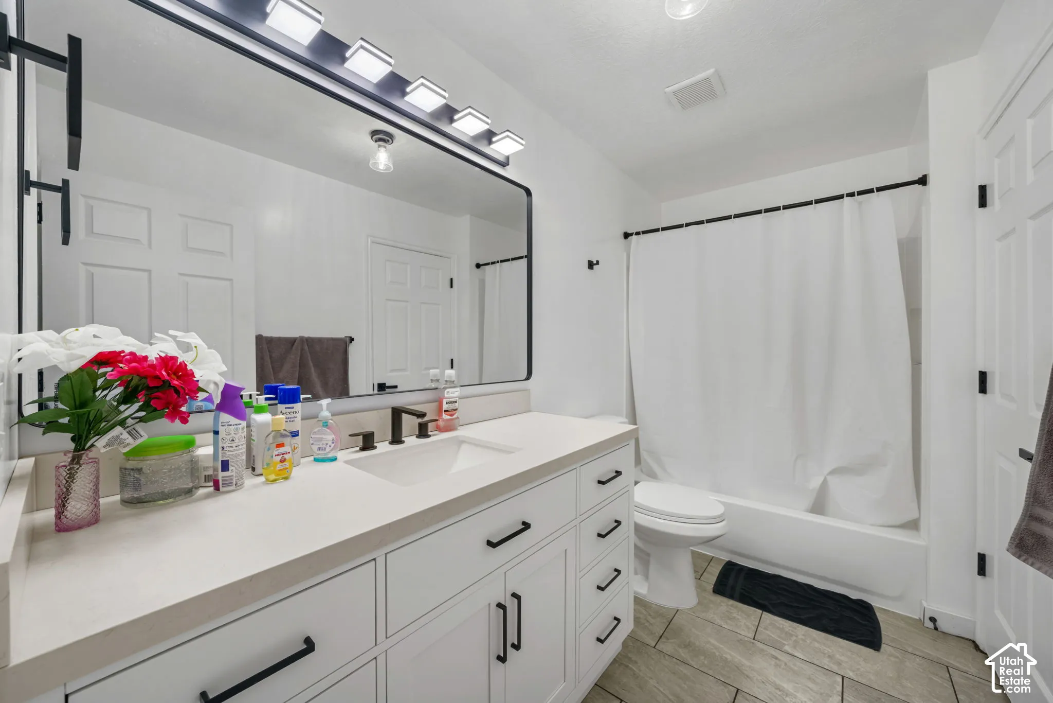 Bathroom featuring a white vanity with matte black hardware, a large rectangular mirror with an integrated light fixture, a wide undermount sink, and wood-finish tile flooring