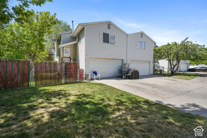 Two-story residential structure featuring light-colored horizontal siding, dual attached garages, a concrete driveway, and a chain-link fenced yard