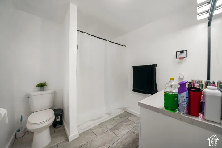 Bathroom featuring a tub-shower combination, grey tile flooring, a white vanity with a neutral countertop, and wall-mounted vanity lighting