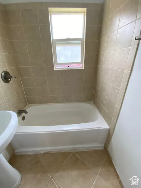 Bathtub with neutral ceramic wall tiling, pedestal sink, single-hung window, and ceramic tile flooring