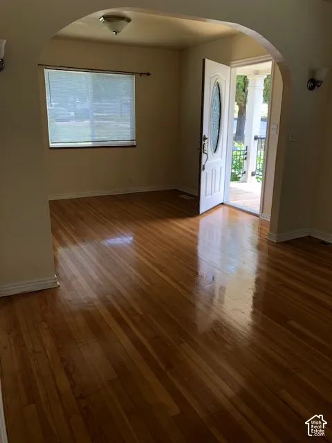 Interior space featuring wood-finish flooring, a decorative arched entryway, a white exterior door with an oval glass insert, and a wall-mounted light fixture