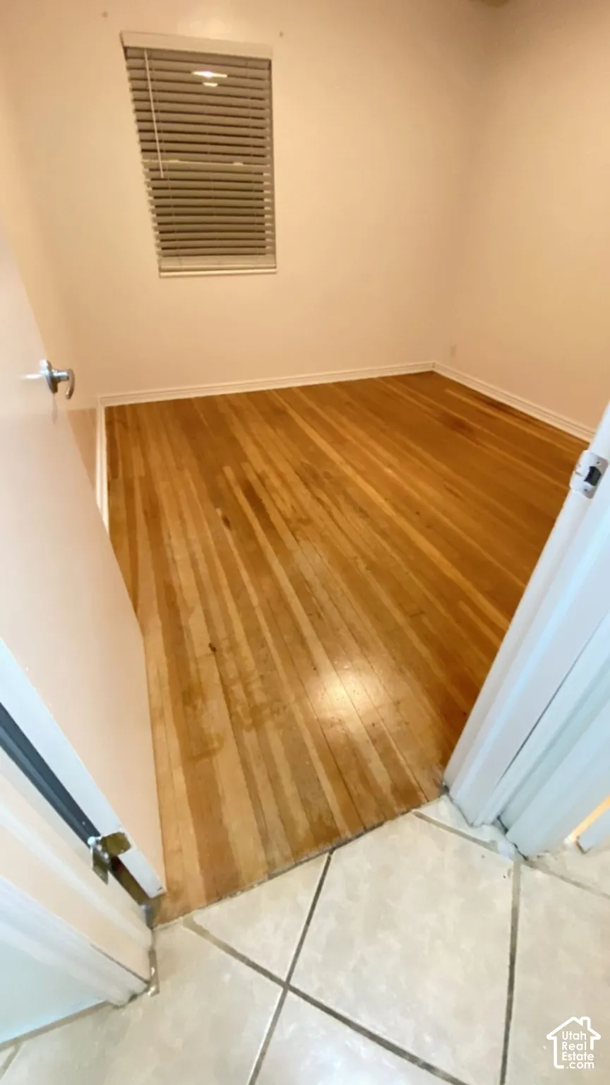 Interior room featuring wood-finish flooring, white walls, and a window fitted with horizontal blinds