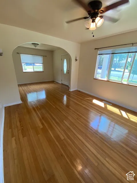 Hardwood flooring, arched architectural opening, multi-light ceiling fan, and large windows with horizontal blinds