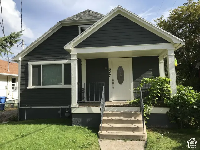 Dark-toned horizontal lap siding exterior featuring a covered front porch, concrete steps with metal railings, and a front door with an oval glass insert