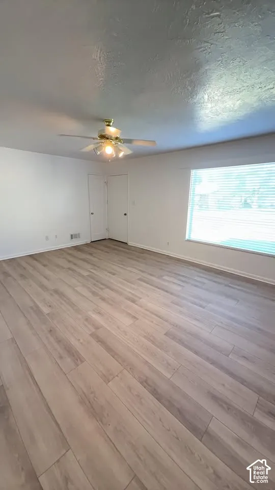 Interior space featuring wood-finish flooring, a ceiling fan with integrated lighting, and a large window with horizontal blinds