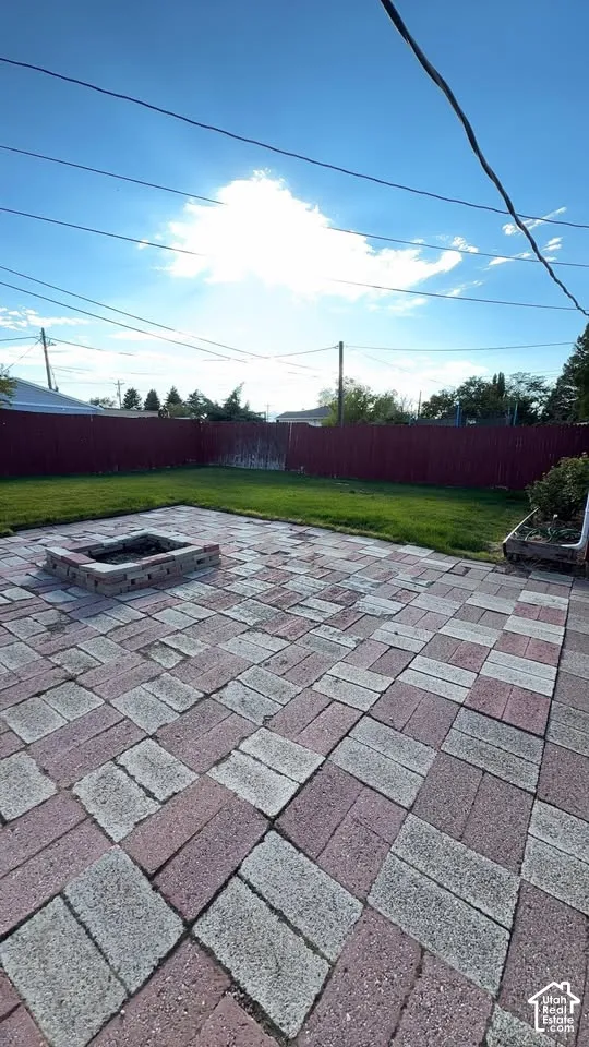 Backyard featuring a paved brick patio, square masonry fire pit, lawn space, and enclosed perimeter fencing