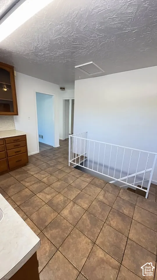 Ceramic tile flooring, built-in wooden cabinetry, white laminate countertops, and a white metal staircase railing