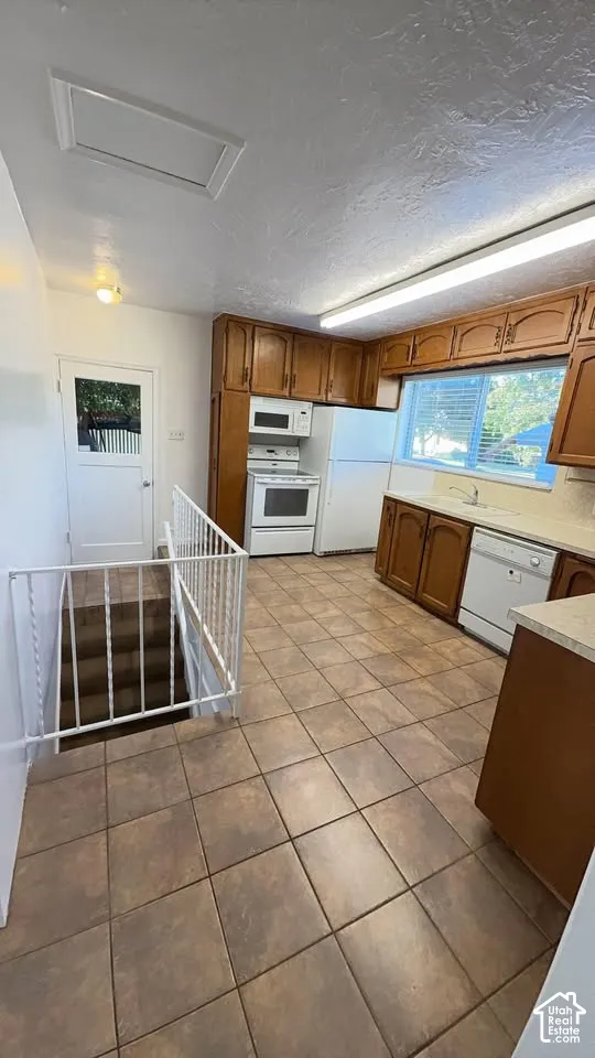 Kitchen featuring wood cabinetry, tile flooring, white appliances, and a metal stair railing