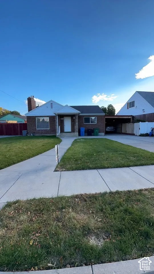Brick exterior home featuring a masonry chimney, gabled roofline, concrete driveway, and attached carport